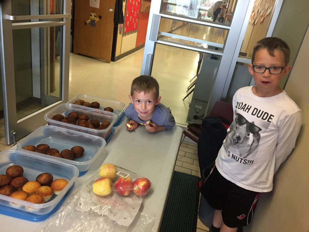 2 boys standing at a table ready to help serving breakfast.